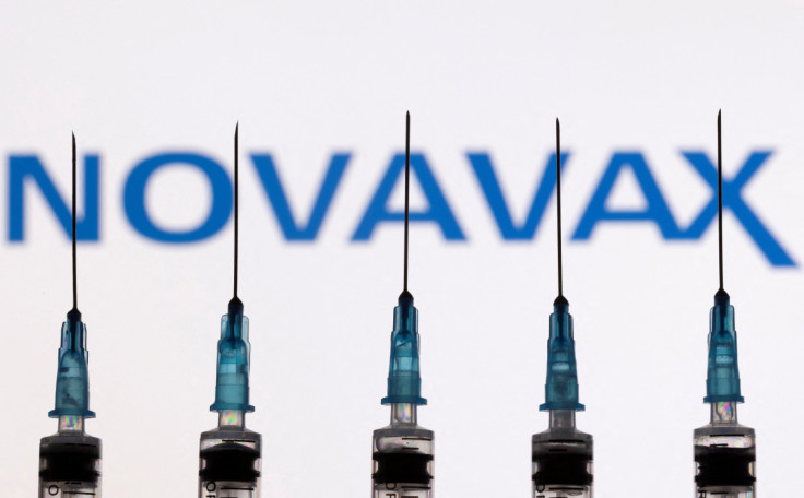 In dieser Abbildung sind Spritzen mit Nadeln vor einem angezeigten Novavax-Logo zu sehen