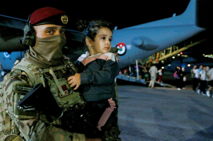 Ein Soldat trägt ein Kind, während Menschen, die aus dem Sudan evakuiert wurden, auf einem Militärflughafen in Amman aus einem Flugzeug aussteigen