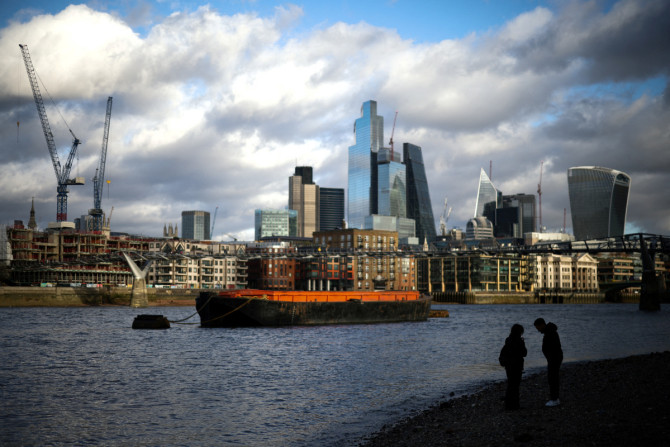In London stehen Menschen am Ufer der Themse, im Hintergrund das Finanzviertel der City of London
